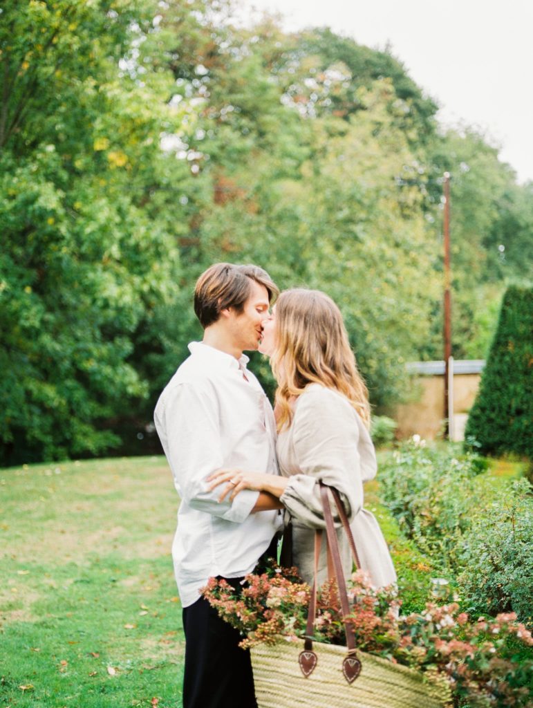 Couple Embracing During a Garden Engagement Session while the girl holds a basket full of flowers