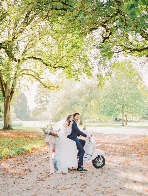 Summer Wedding Portrait of Couple sitting on a white scooter. Bride is leaning on Groom's Back