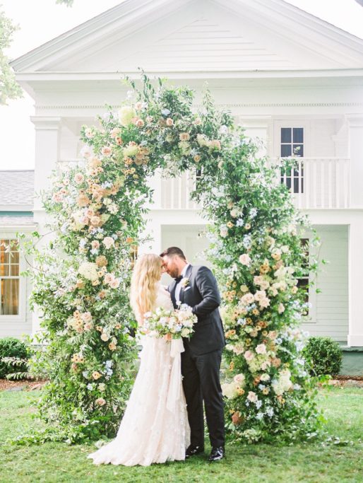 Wedding portrait of a Couple embracing in front of a large floral arch at Zingermans Cornman Farm