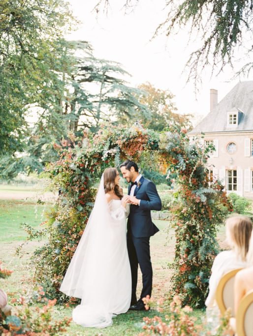 Bride and Groom celebrating after their ceremony in front of a large floral arch at Chateau de Bouthonvilliers in France