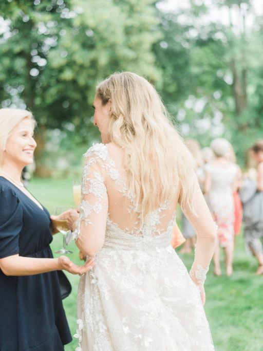Bride in a Lace, Long Sleeve Galia Lahav gown talking to a guest during her wedding reception at Zingerman Cornman Farms